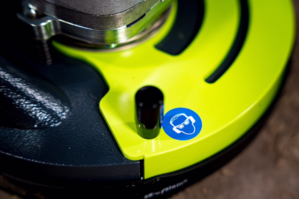 WOLFF_Application Images_BS 180_2024-01 (14) A close-up image of a bright green power tool, showing part of its control panel. A black cylindrical component is prominently visible, next to a blue sticker featuring an icon of a person wearing glasses and headphones, indicating the need for hearing protection.