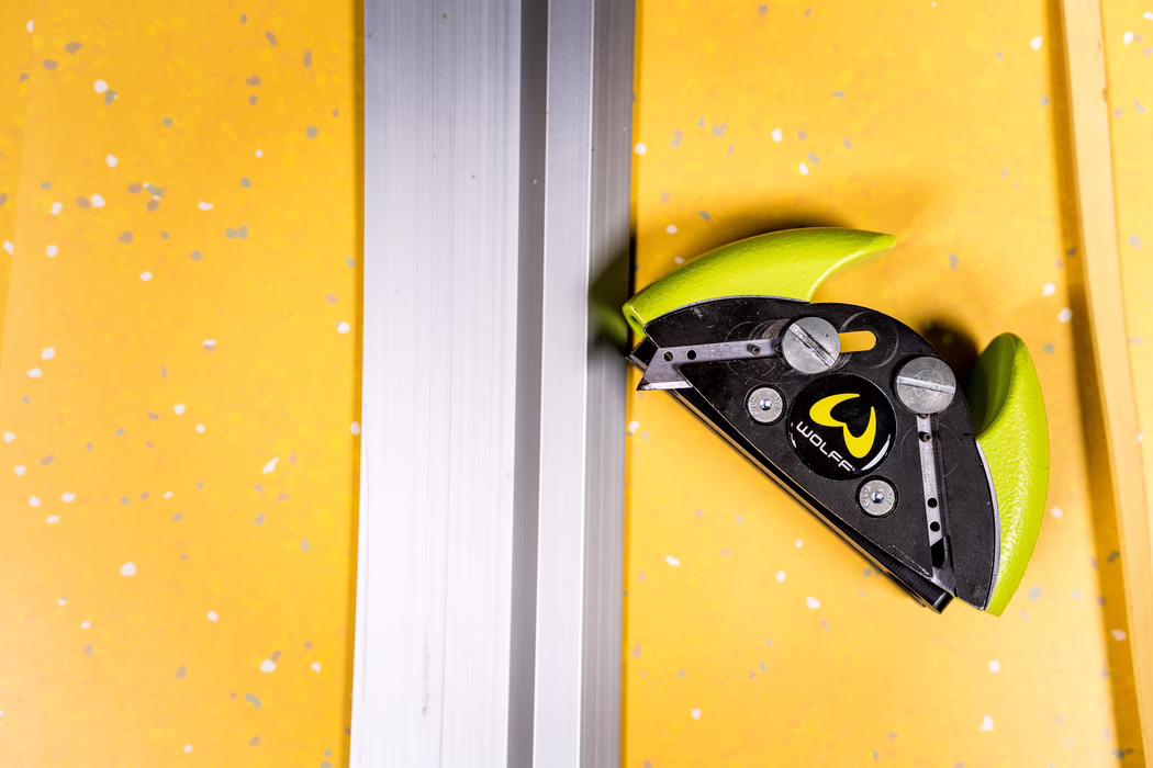 WOLFF_Application Image_Railcut_Detail4_2022-11 Close-up of a green corner clamp attached to a silver aluminum rail on a yellow speckled surface.