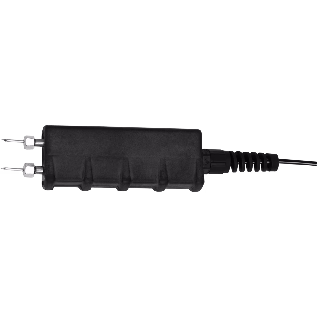 Close-up of a black rectangular electrical connector or inline splice housing photographed against a white background. The component shows two metal pins with hex nuts on the left, a molded plastic body with ribbed contours in the center, and a cable gland with a flexible strain-relief boot on the right where a black insulated cable exits. The image is tightly cropped and studio-lit, emphasizing the connector's mechanical details, textures and assembly features.